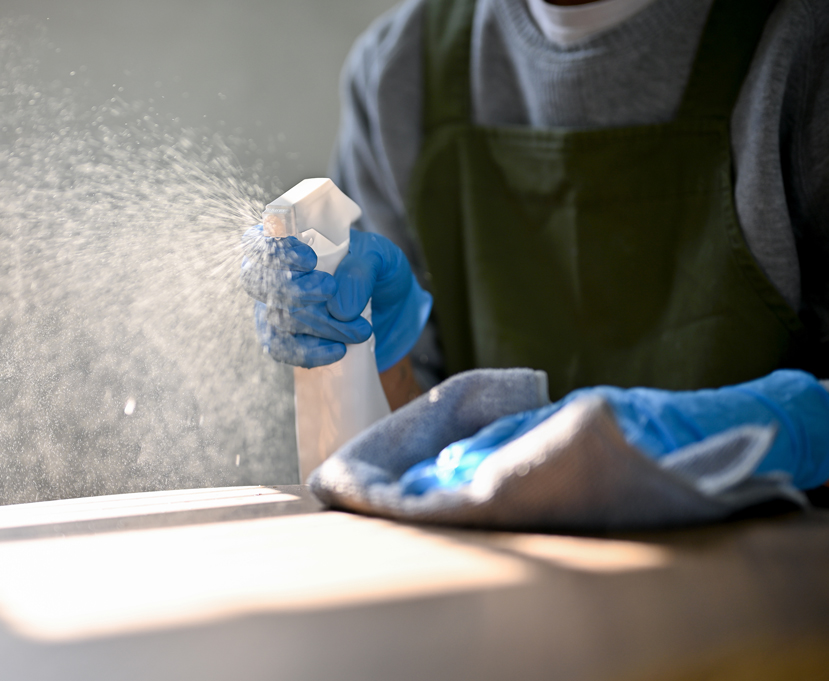 Hombre con guantes de goma limpiando mesa con paño azul y spray